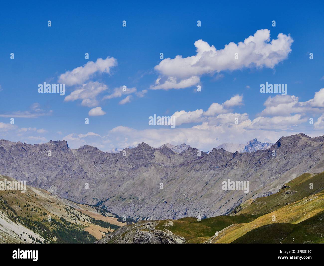Paysage de montagne alpin avec des pentes rocheuses, de l'herbe sauvage et un ciel bleu sur des sommets lointains Banque D'Images