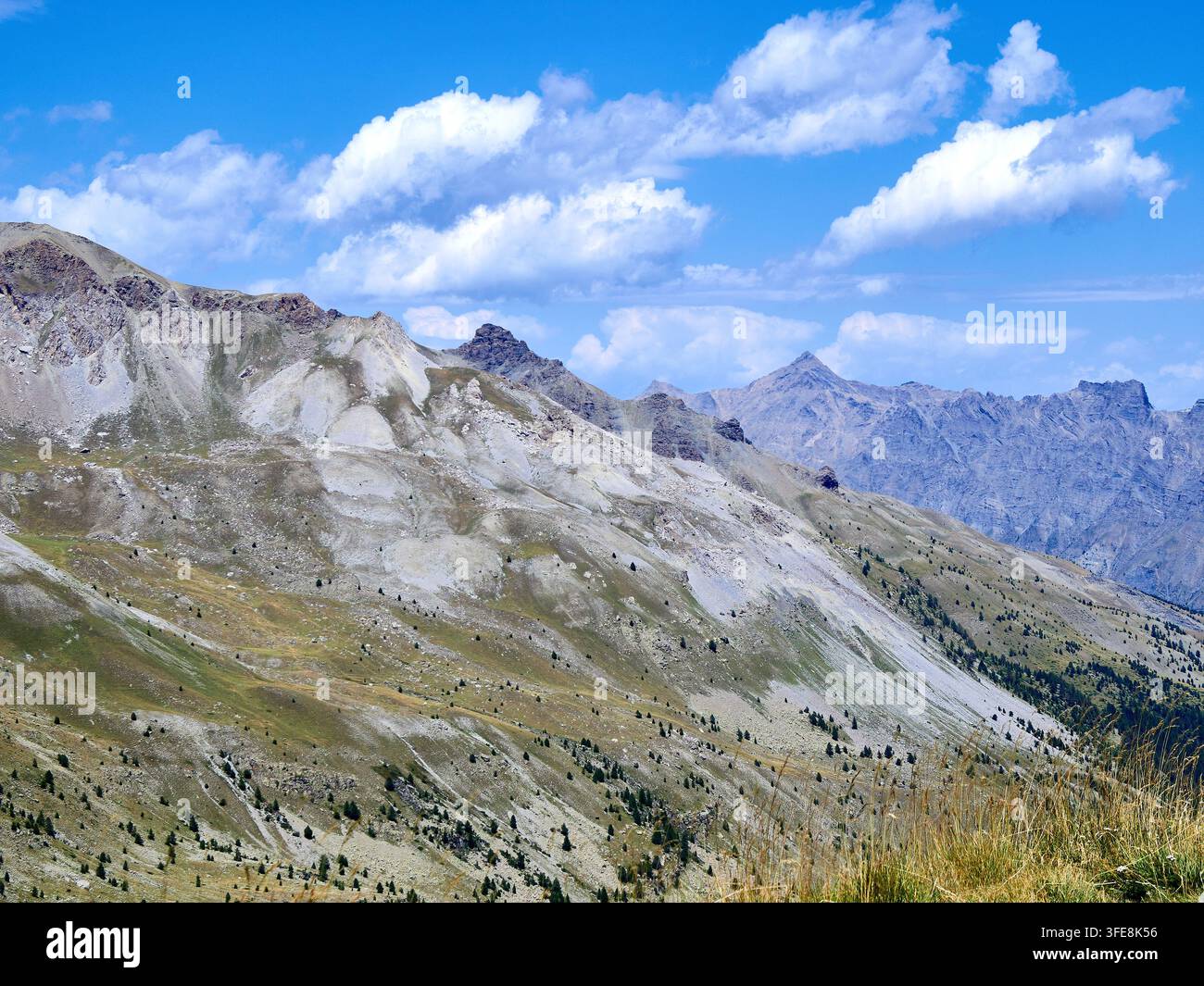 Paysage de montagne alpin avec des pentes rocheuses, de l'herbe sauvage et un ciel bleu sur des sommets lointains Banque D'Images