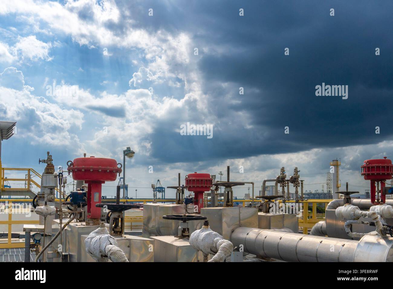 Vannes de contrôle rouges montées sur des tuyaux blancs isolés dans une installation de gaz portuaire avec des nuages d'orage dramatiques et un ciel bleu en arrière-plan et port Banque D'Images