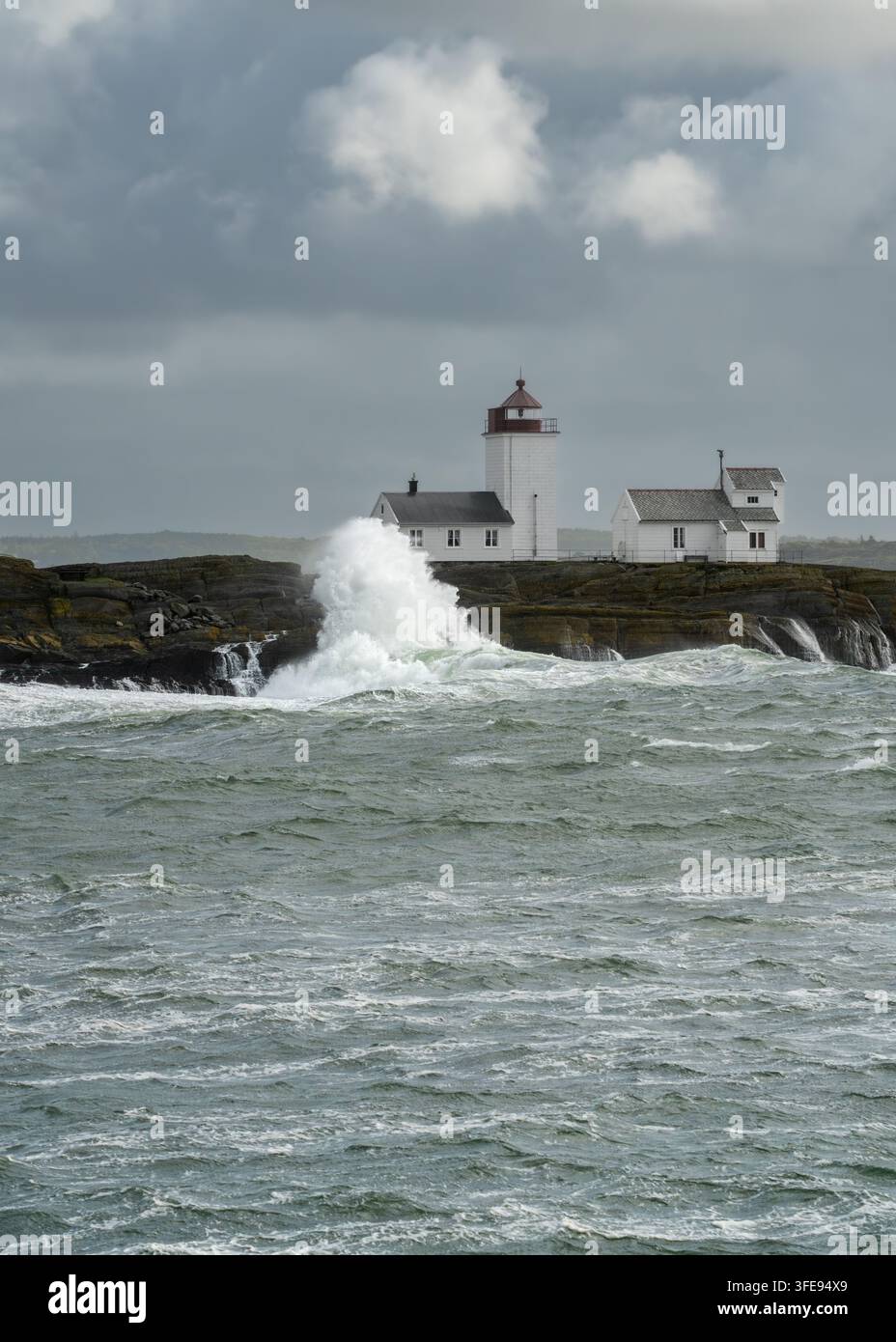L'impact des vagues sur un phare s'élève en une haute colonne d'eau à côté du phare de Langoytangen au-dessus des eaux agitées de la mer du Nord en Norvège pour la résilience maritime, la navigation Banque D'Images