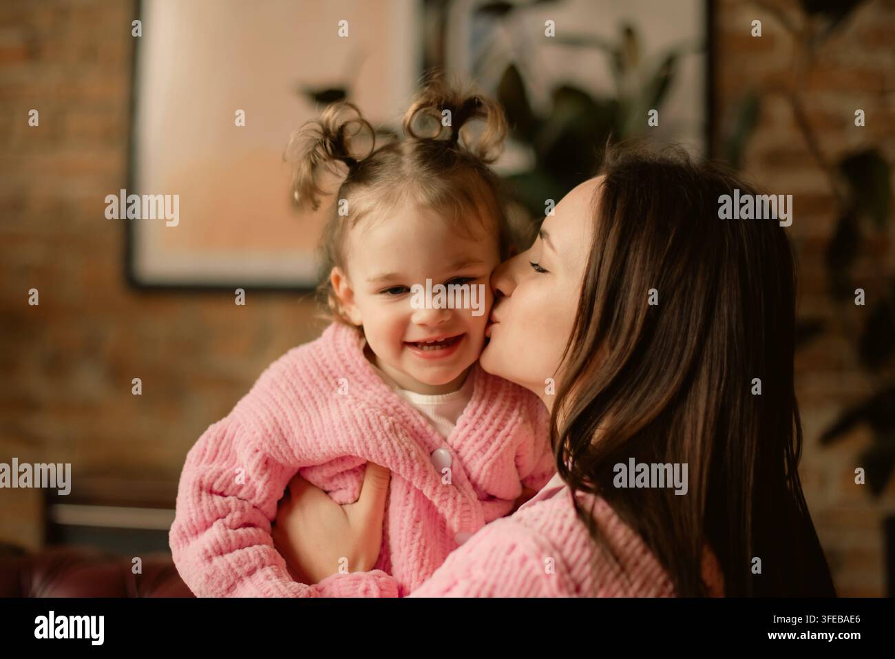 Mère aimante embrassant la joue de sa mignonne petite fille portant des pulls roses assortis Banque D'Images