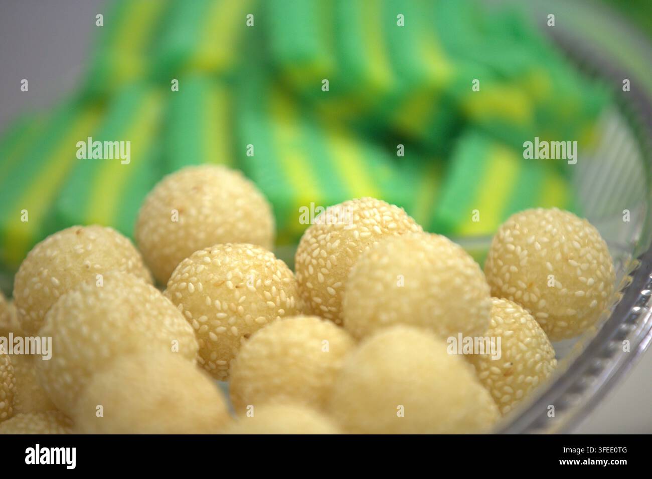 Close-up de snacks asiatiques traditionnels, mettant en avant des boules de sésame frites dorées (onde-onde) avec un gâteau Kue lapis rayé de vert en arrière-plan. Banque D'Images