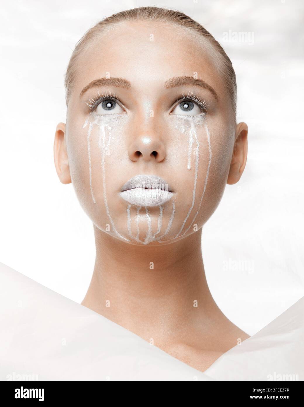 Modèle féminin avec un maquillage artistique du visage blanc et des larmes, posant devant un fond clair, mettant en valeur un concept de beauté unique avec un maquillage dramatique Banque D'Images