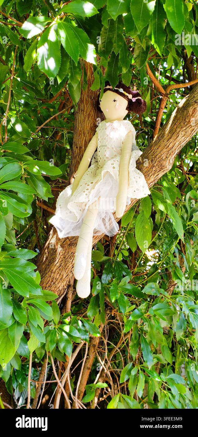 Poupée en tissu faite à la main assise dans un arbre entourée de feuilles vertes Banque D'Images