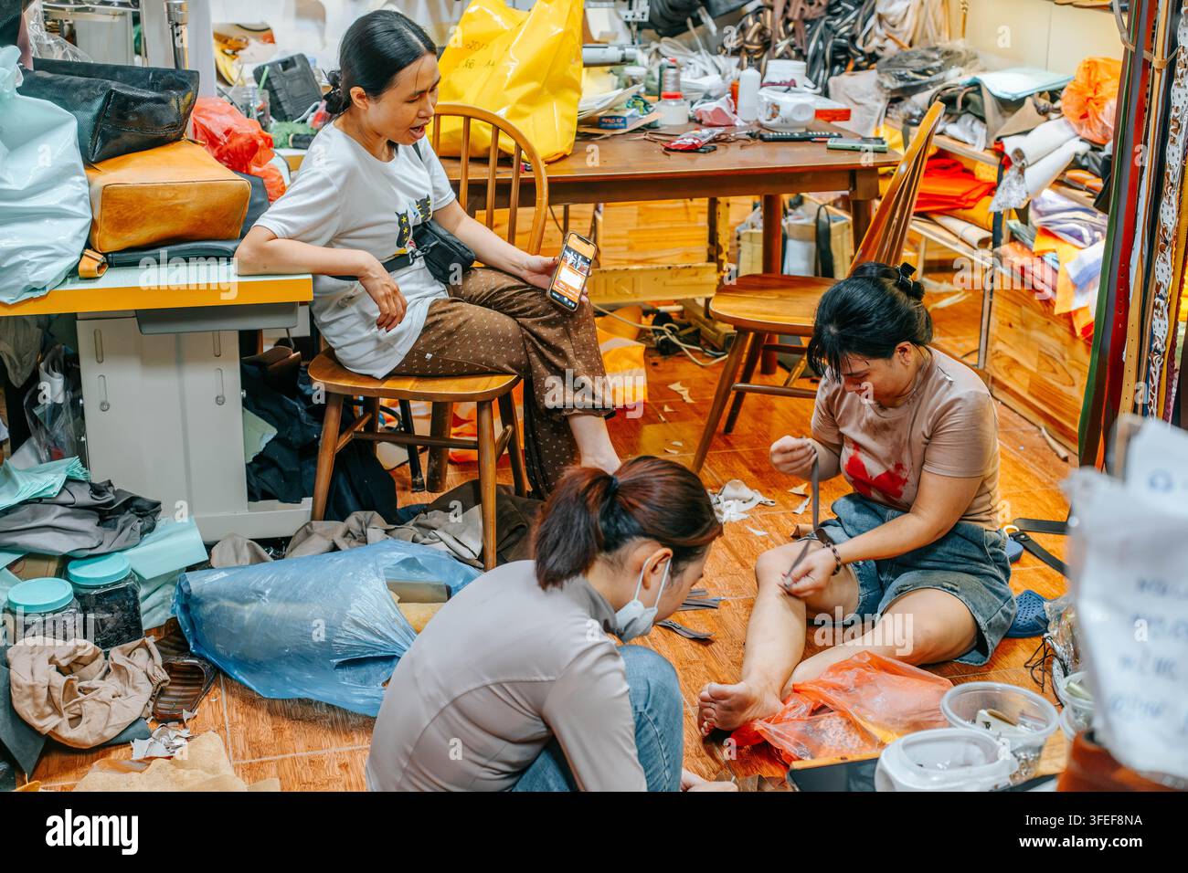 Hoi An, Vietnam - 27 août 2026. Trois femmes travaillent ensemble sur des articles en cuir dans un atelier animé rempli d’outils, de matériaux et de produits artisanaux Banque D'Images