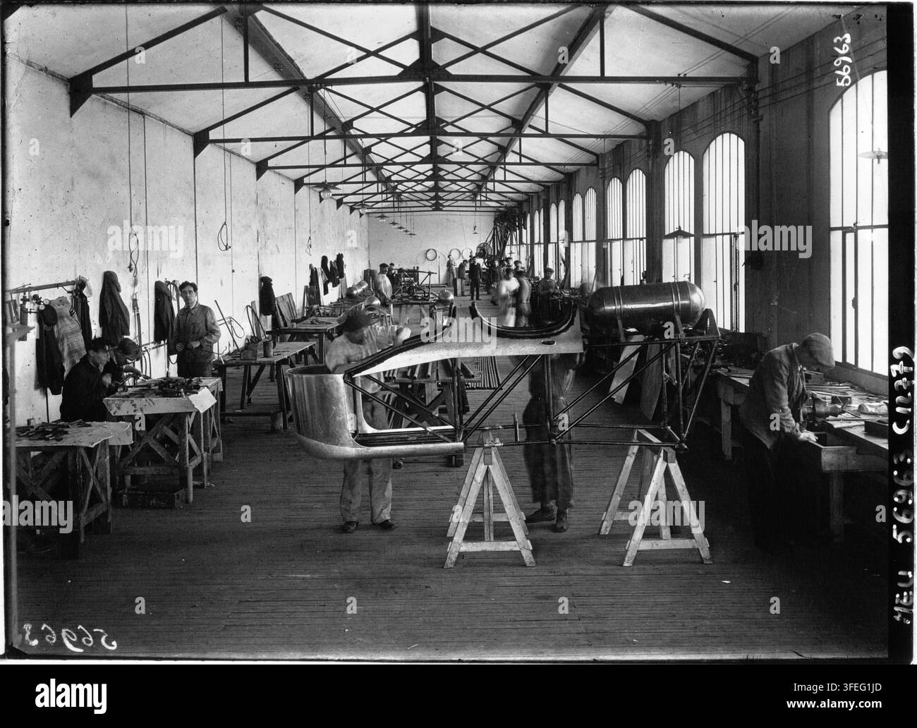 Une photographie de presse de 1915 sur la fabrication d'avions chez Darracq, montrant des ouvriers assemblant de grandes structures métalliques ou en bois incurvées sur des établis en bois dans un long atelier intérieur avec un haut plafond à charpente et de grandes fenêtres en arc, par Agence Meurisse, une agence de photographie de presse française. Banque D'Images