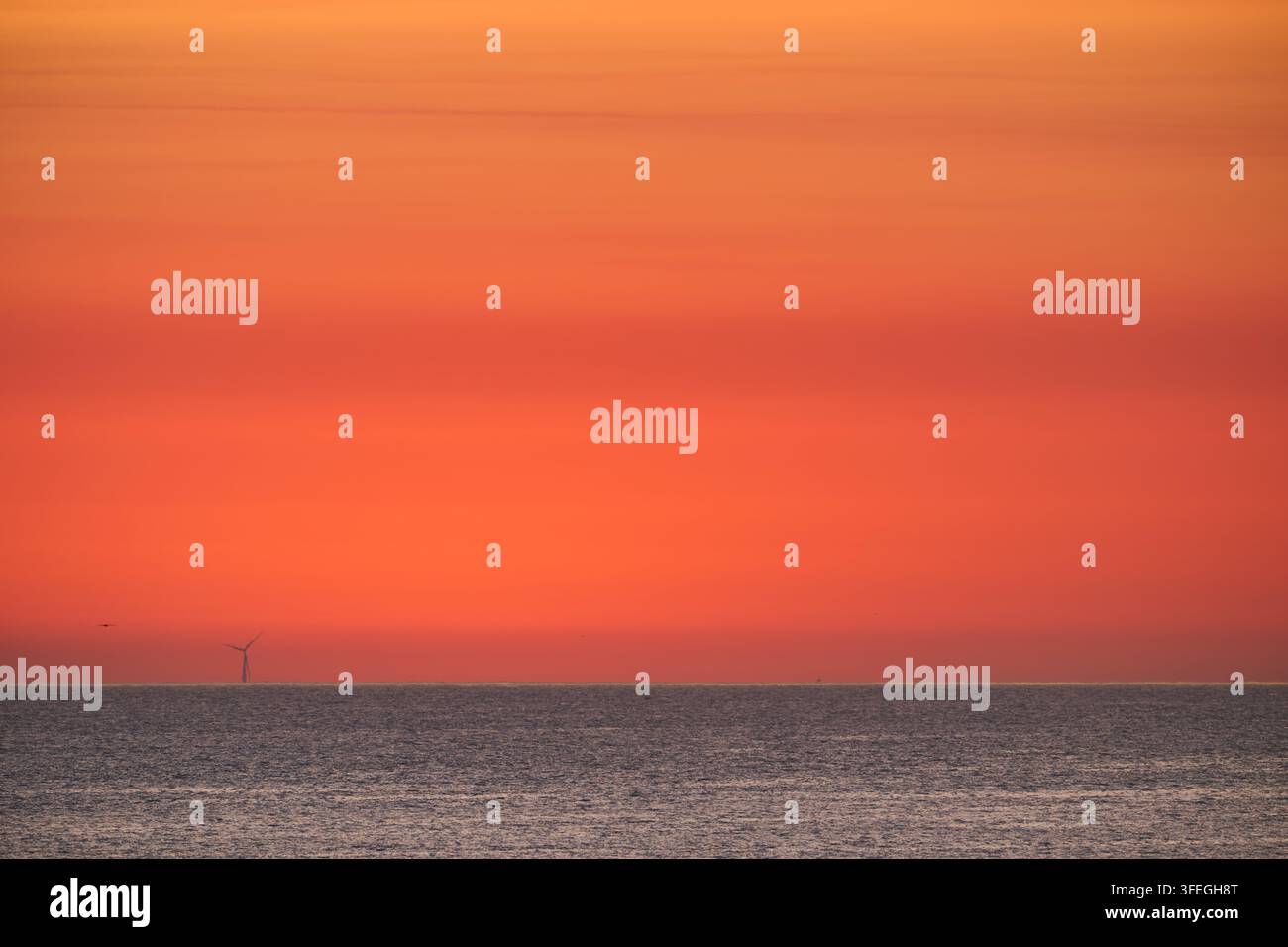 Éolienne isolée à l'horizon contre un ciel de coucher de soleil orange et rouge vif, reflétant l'harmonie paisible de l'énergie renouvelable et de la nature Banque D'Images