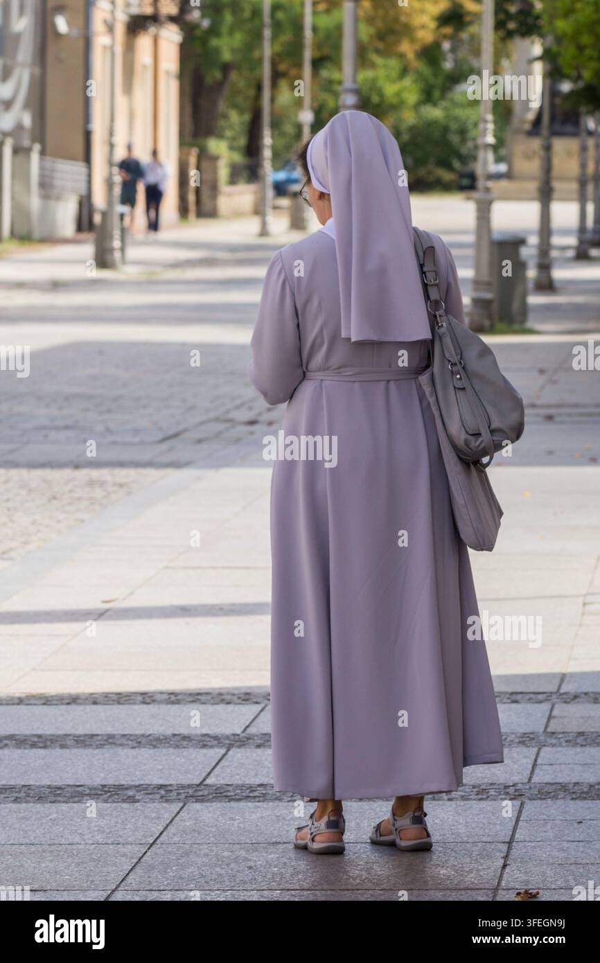 Nun dans un long habit gris marchant le long d'un trottoir urbain, portant un sac à épaule dans un cadre urbain Banque D'Images