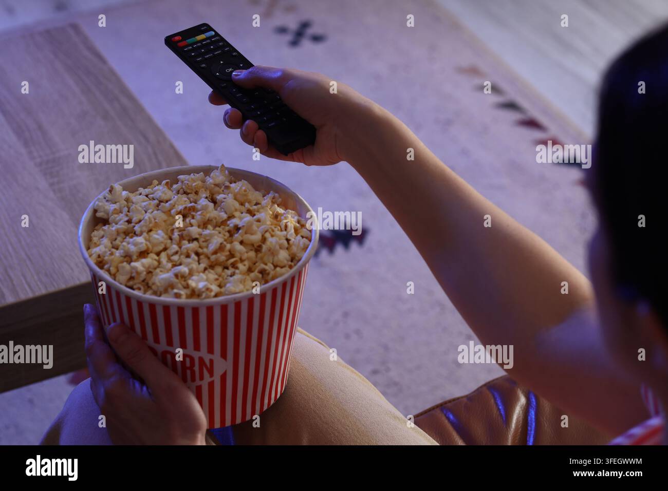 Divertissement et loisirs à la maison, personne regardant des films avec du pop-corn et une télécommande dans un salon confortable la nuit avec une lumière bleue cinématographique Banque D'Images