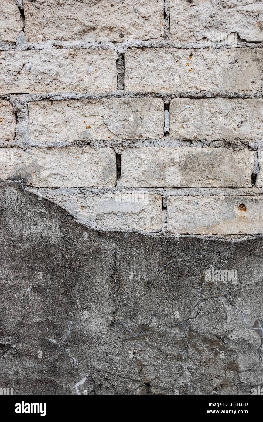 mur de maçonnerie érodé avec des briques pâles, du mortier endommagé et un enduit gris fissuré, montrant la dégradation, la réparation et la texture vieillotte du bâtiment Banque D'Images