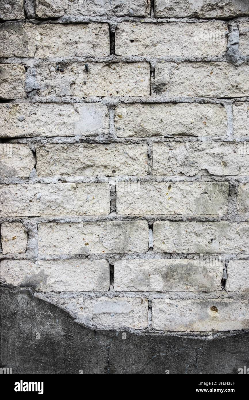 mur de maçonnerie érodé avec des briques pâles, du mortier endommagé et un enduit gris fissuré, montrant la dégradation, la réparation et la texture vieillotte du bâtiment Banque D'Images