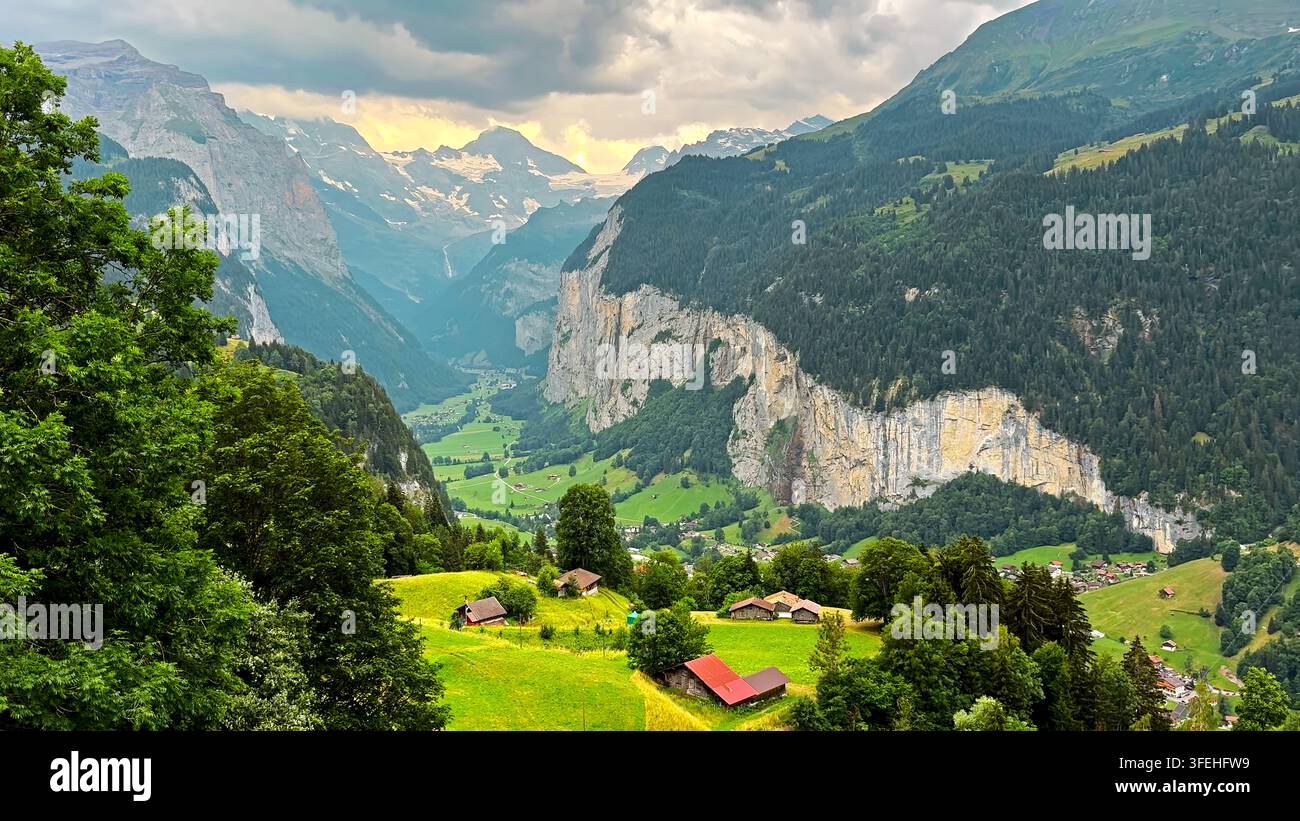 Vallée alpine suisse dramatique sous des sommets ennuagés. Vallée alpine suisse verte avec prairies, chalets, falaises abruptes, forêts et cimes enneigées Banque D'Images