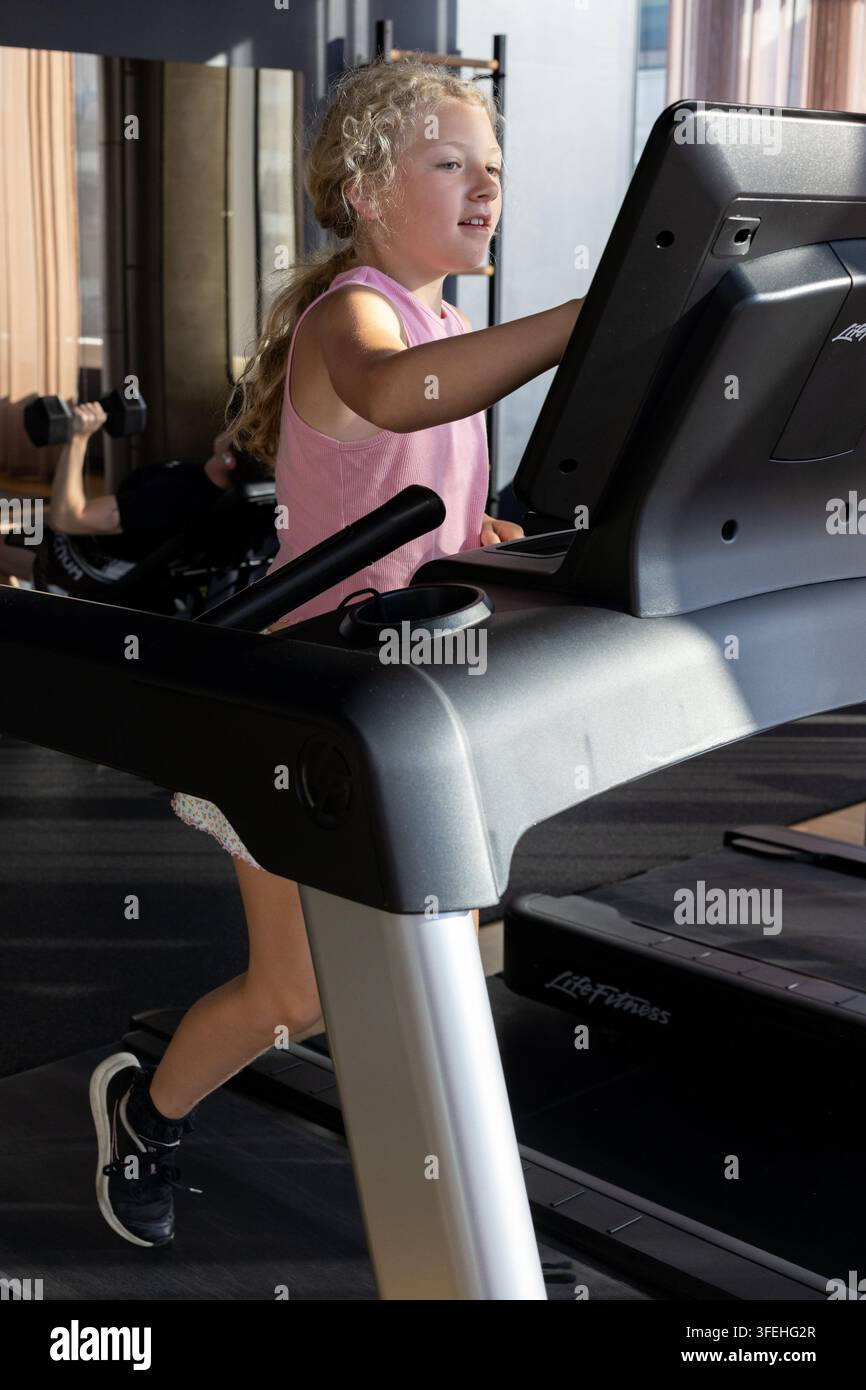 Une fille blanche de dix ans courant sur un tapis de course dans une salle de sport Banque D'Images