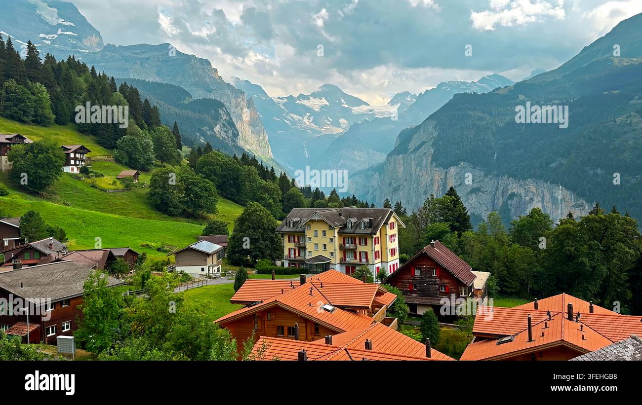 Village alpin suisse surplombant une vallée montagneuse spectaculaire. Village alpin suisse avec des chalets en bois et des toits rouges surplombant une vallée montagneuse luxuriante Banque D'Images