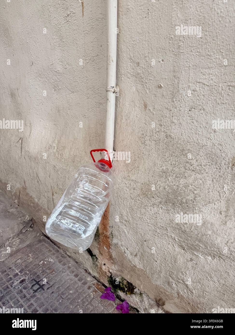 Sousse, Tunisie, 2026. Un système improvisé de collecte d'eau de pluie fabriqué à partir d'une bouteille en plastique sous un tuyau d'écoulement dans la médina de Sousse, illustrant l'adaptation quotidienne à la crise grave de l'eau en Tunisie, à la pénurie chronique d'eau et aux coupures récurrentes d'approvisionnement de plus en plus intensifiées par la chaleur extrême et le changement climatique Banque D'Images
