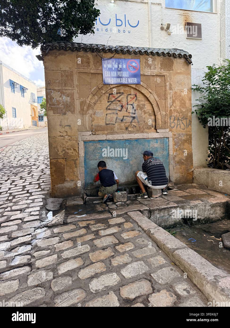 Tunis, Tunisie, 2026. Les gens cherchent un soulagement face à la chaleur extrême de l'été à une fontaine publique marquée « eau non potable / eau non buvable », au milieu de pénuries d'eau graves et de coupures récurrentes d'approvisionnement dans la crise hydrique s'aggravant en Tunisie, intensifiée par une pénurie chronique et le changement climatique Banque D'Images