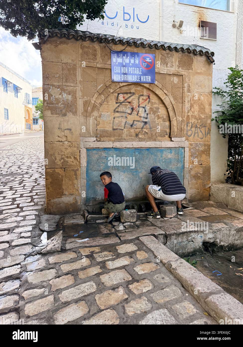 Tunis, Tunisie, 2026. Les gens cherchent un soulagement face à la chaleur extrême de l'été à une fontaine publique marquée « eau non potable / eau non buvable », au milieu de pénuries d'eau graves et de coupures récurrentes d'approvisionnement dans la crise hydrique s'aggravant en Tunisie, intensifiée par une pénurie chronique et le changement climatique Banque D'Images
