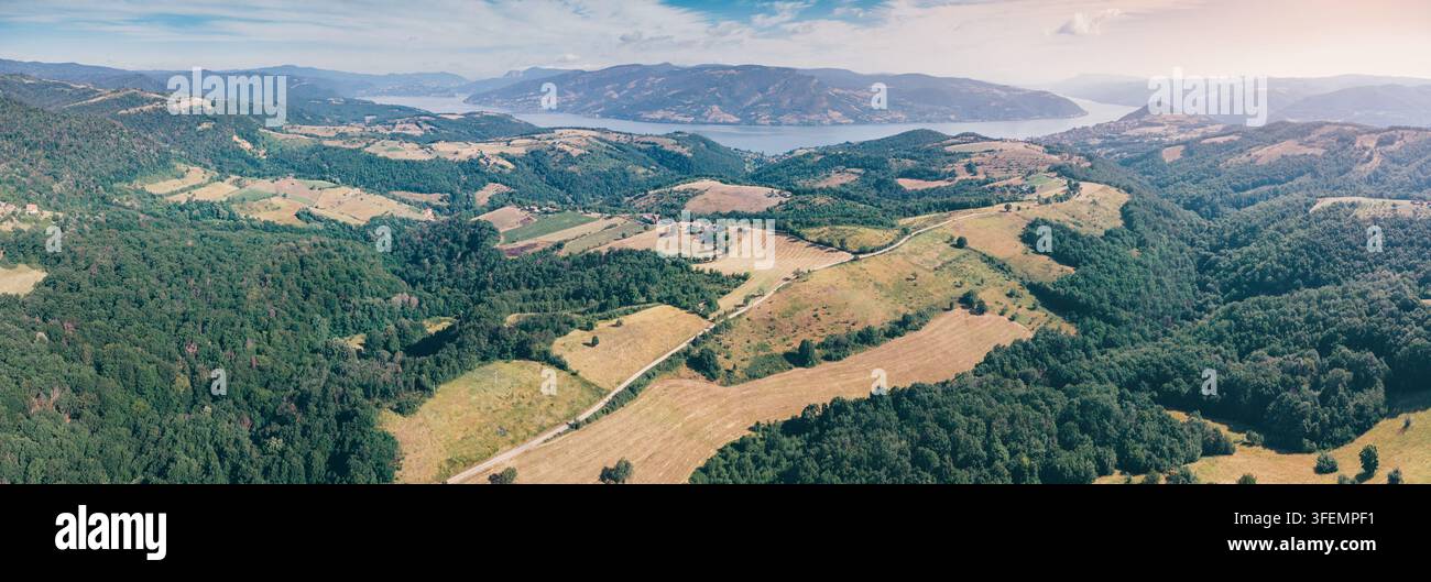 Panorama aérien étendu de terres agricoles ondulantes, de collines boisées et d'un lac lointain scintillant sous un ciel estival brumeux, évoquant un paysage inexploré Banque D'Images