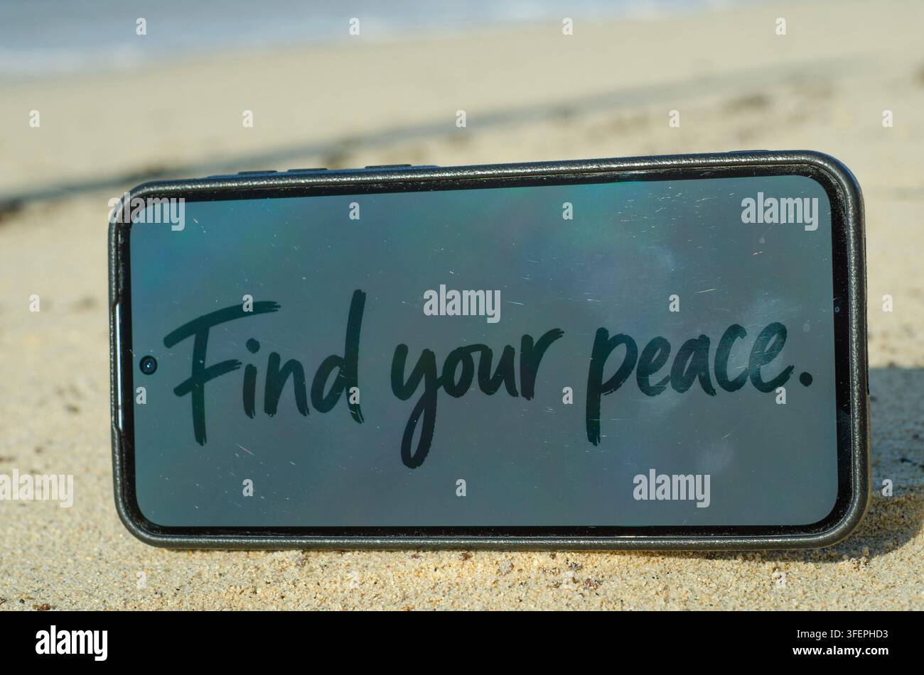 Un smartphone affiche un message de motivation "Trouve ta paix" posé sur une plage de sable suggérant la tranquillité et une échappée numérique Banque D'Images