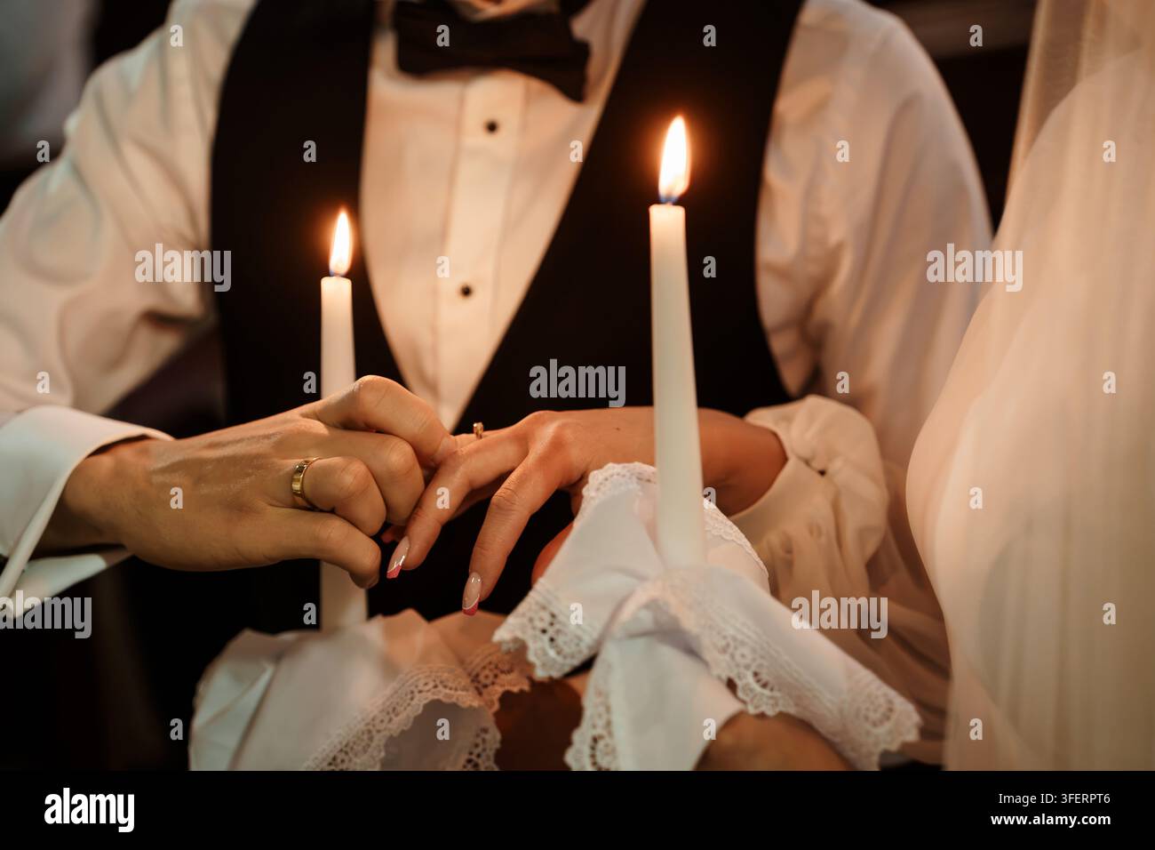 Marié plaçant une alliance au doigt d'une mariée lors d'une cérémonie traditionnelle à la lumière des bougies, capturant l'intimité et l'engagement à vie Banque D'Images