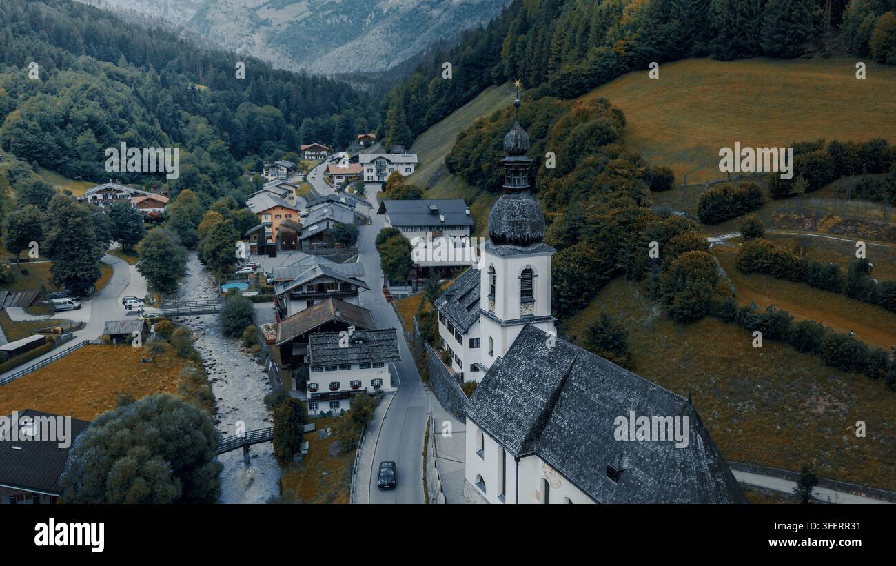 Vue aérienne de l'église paroissiale Saint-Sébastien entourée de maisons alpines traditionnelles, d'une rivière qui coule et de pentes montagneuses vertes luxuriantes, Ramsau près de Banque D'Images