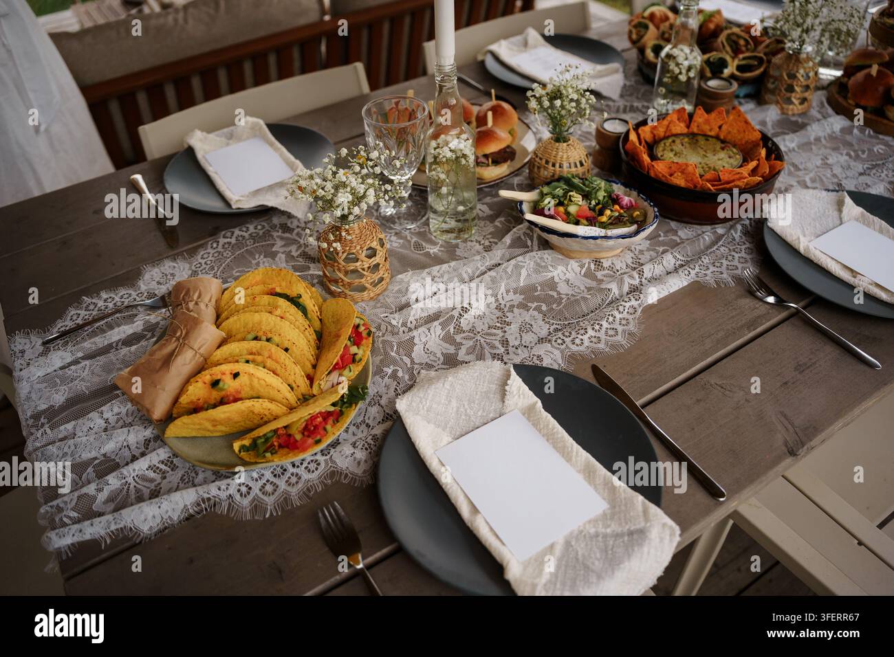 Table de salle à manger extérieure rustique dressée pour un festin d'été avec tacos, burgers et salade fraîche, nappe en dentelle élégante, parfaite pour les concepts d'événement et de fête Banque D'Images