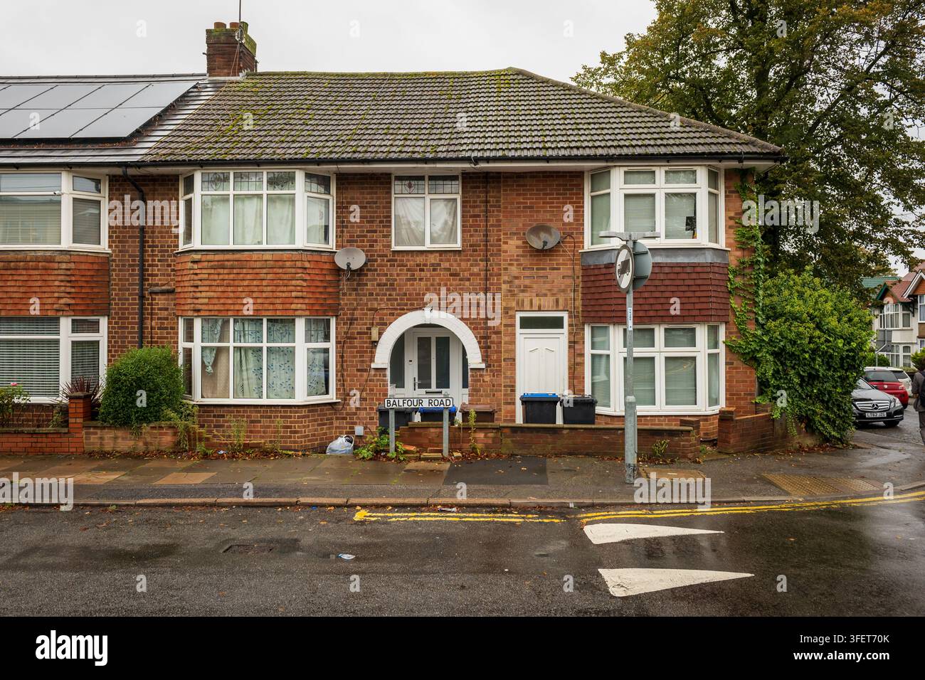 Maison mitoyenne en briques rouges sur Balfour Road à Northampton, Royaume-Uni, dotée de baies vitrées, de dishes satellites, de poubelles avant et d’un trottoir mouillé après la pluie Banque D'Images