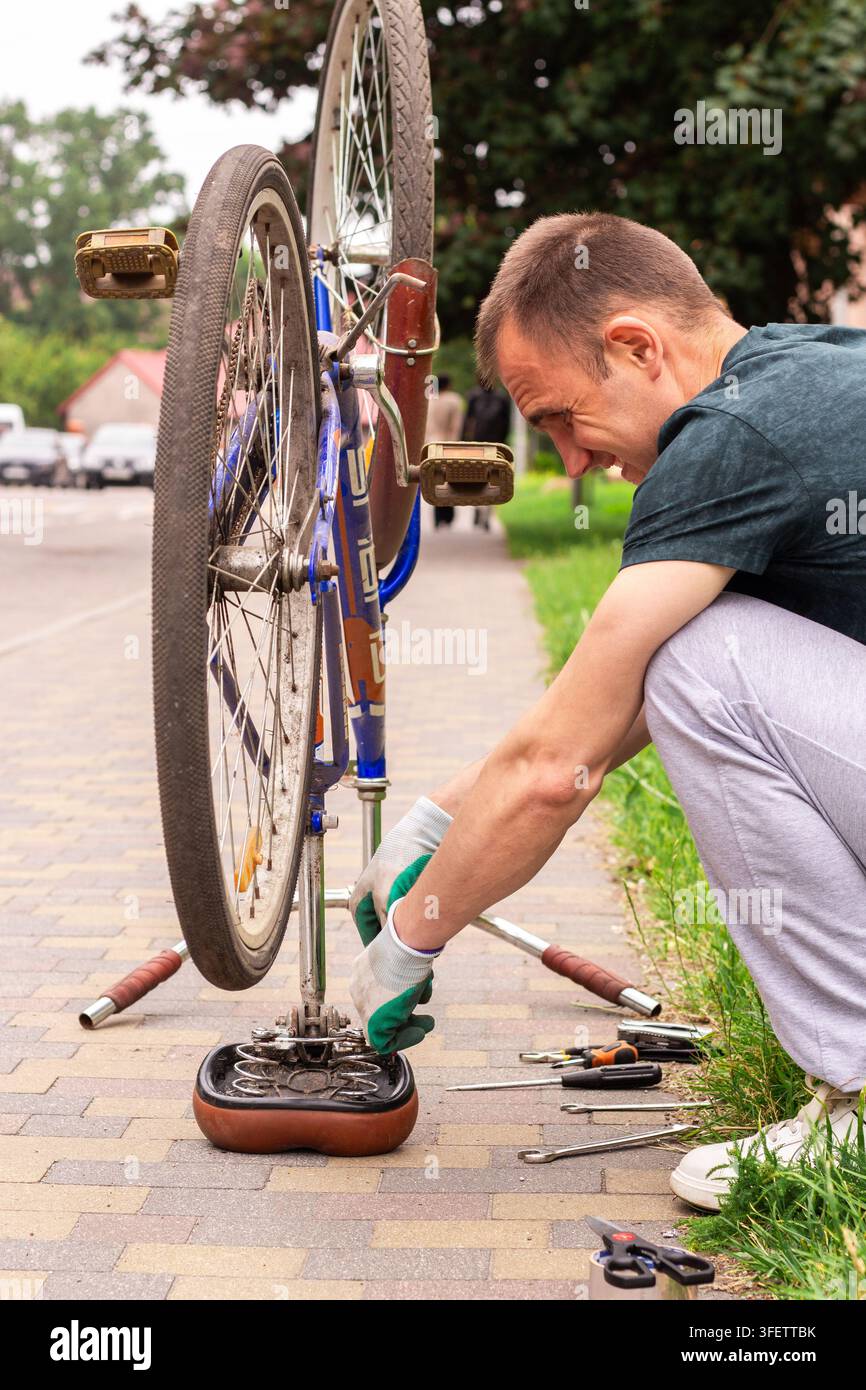 Homme retournant le vélo à l'envers devant la maison. Vérification des roues et de la chaîne pour détecter les dommages. La réparation du vélo montre l'autonomie. Préparation saisonnière pour les balades d'été Banque D'Images
