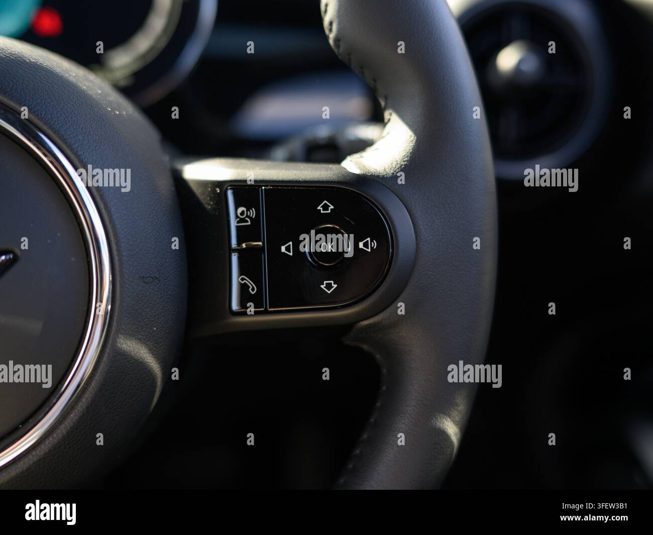 Grossissement du panneau de contrôle du volant de voiture. Le volant en cuir noir domine le cadre. Un emblème circulaire apparaît sur le côté gauche. Médias et ph Banque D'Images