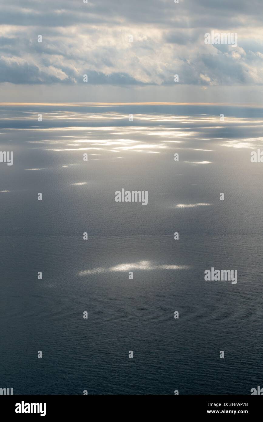La lumière du soleil perce les nuages au-dessus de la mer Tyrrhénienne, en Italie, créant des taches scintillantes de lumière réfléchie à la surface de l'eau. Banque D'Images