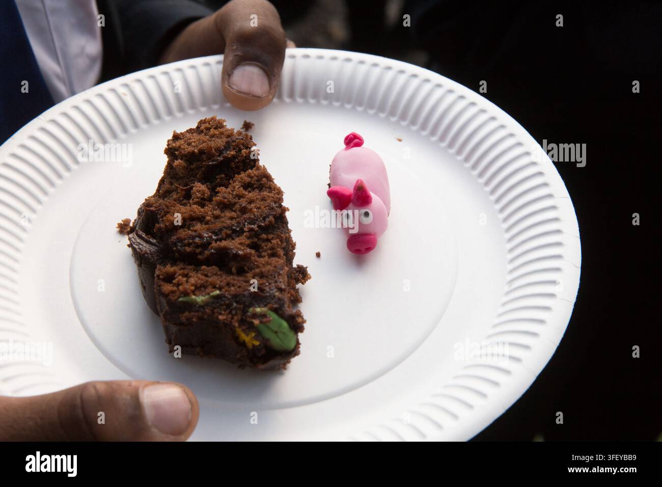 Une personne tient une assiette en carton avec une part de gâteau "porcs dans la boue" et un cochon en pâte à modeler pour savourer une douceur lors d'une vente de pâtisseries communautaire. Banque D'Images