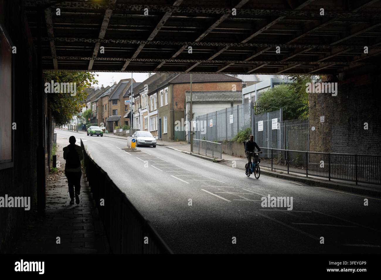 Un piéton et un cycliste font leur trajet sous un pont ferroviaire à Wandsworth, Londres, en empruntant les rues locales pour leurs déplacements quotidiens. Banque D'Images