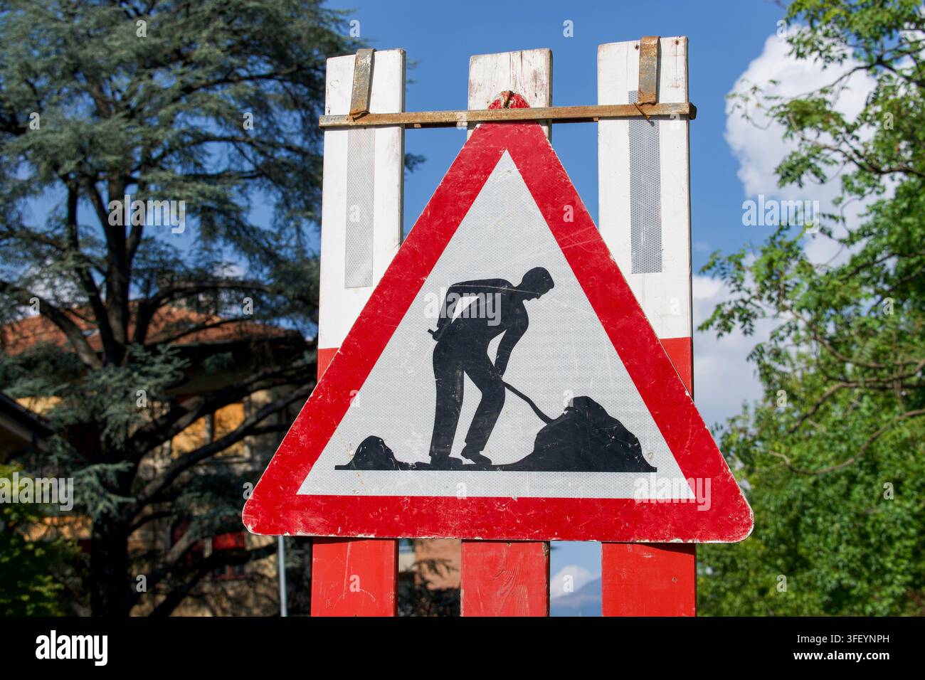 Panneau d'avertissement de travaux routiers sur une barrière de chantier en bois entourée d'arbres verts et d'un ciel bleu. Concept pour la construction routière Banque D'Images
