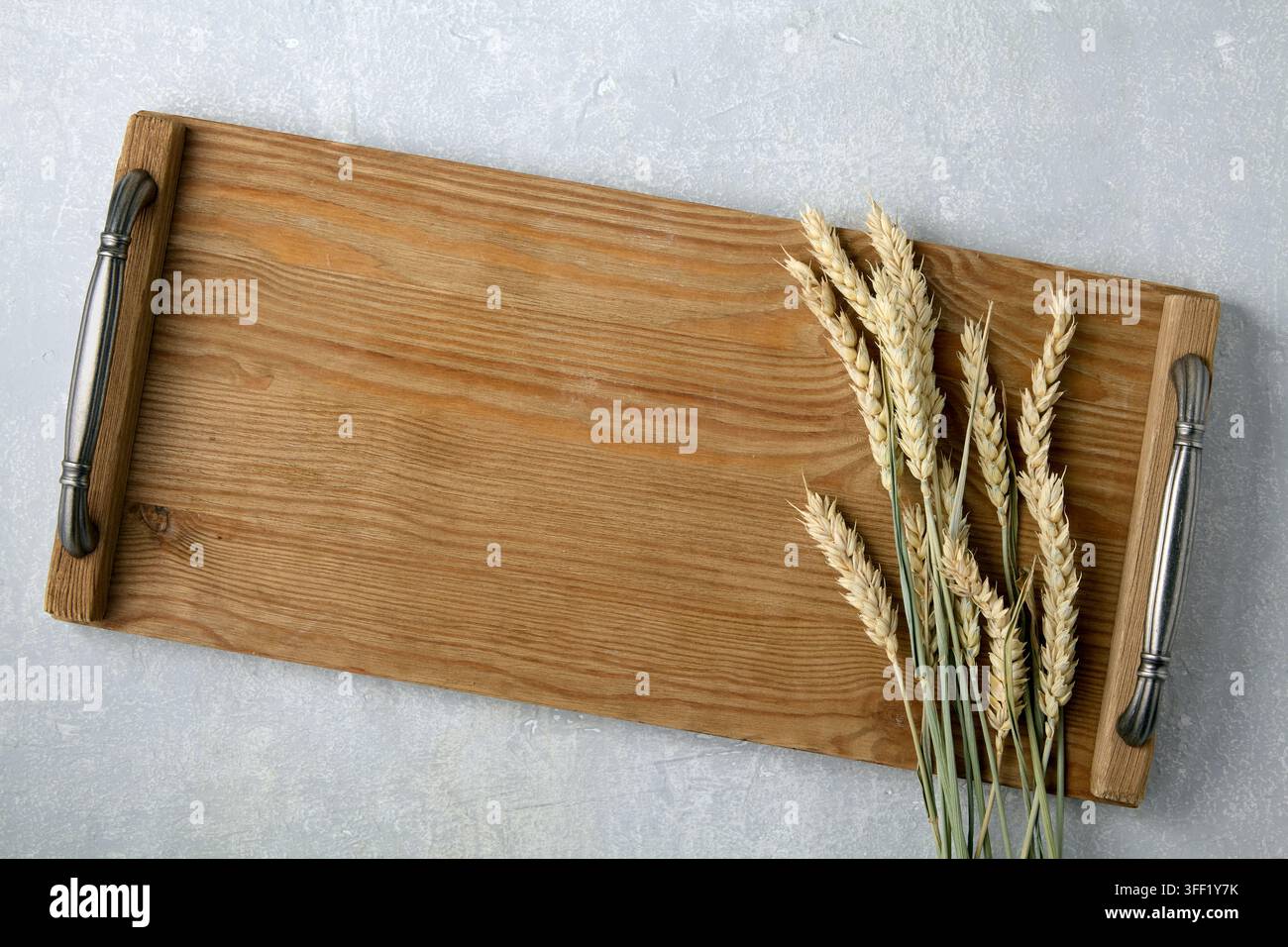 Un plateau en bois marron vide, une planche avec des poignées et des épis de blé sur une table en pierre grise. Vue de dessus avec espace de copie. Banque D'Images