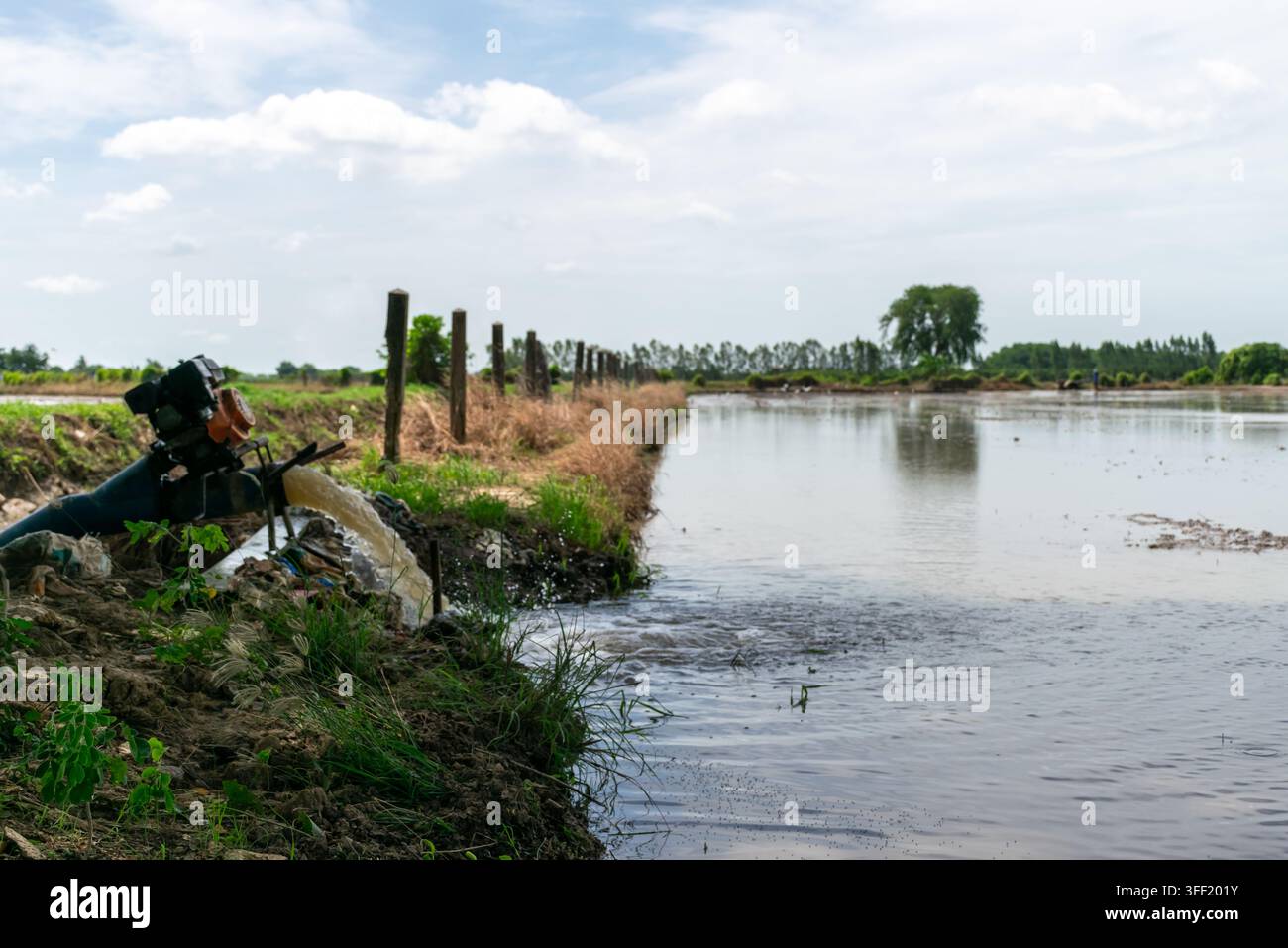Pompe à eau motorisée déversant dans un champ agricole inondé pour l'irrigation des cultures, le drainage et la gestion de l'eau douce dans un paysage agricole rural Banque D'Images