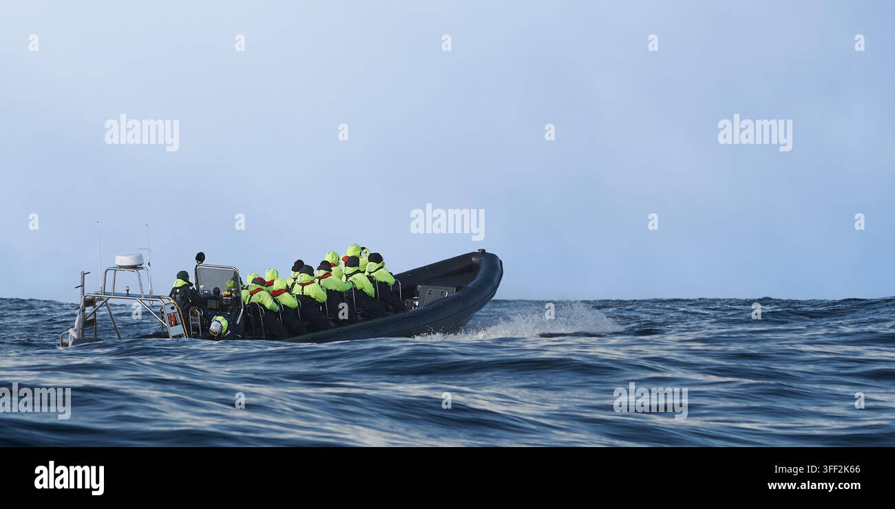 Bateau touristique gonflable transportant des touristes à travers la mer de Norvège lors d'une excursion d'observation de la faune. Les passagers portent des vêtements de protection colorés Banque D'Images