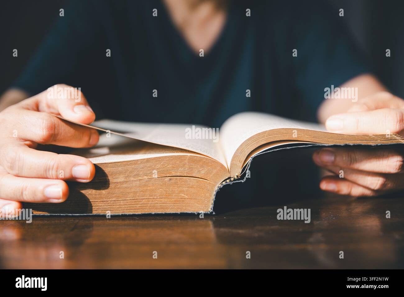 Gros plan de mains tournant les pages d'une ancienne Bible sur une table en bois, représentant la lecture des Écritures chrétiennes, l'étude de la foi, la dévotion, l'adoration, le spirituel Banque D'Images