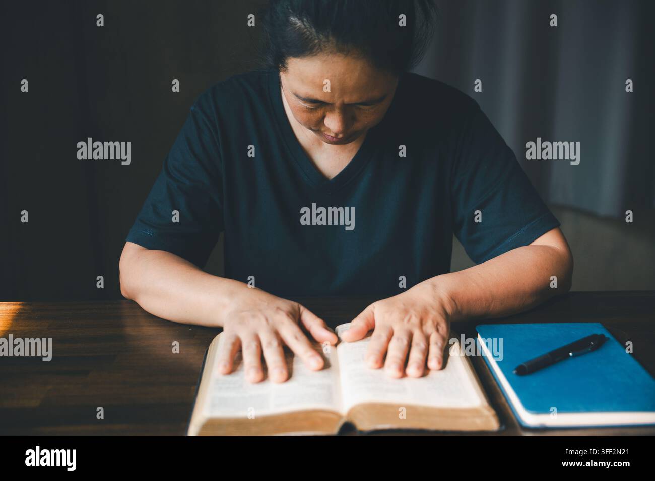 Personne adulte reposant ses deux mains sur une Bible ouverte à côté d'un carnet et d'un stylo, représentant l'étude des Écritures, la foi chrétienne, la dévotion, la prière, la réflexion Banque D'Images