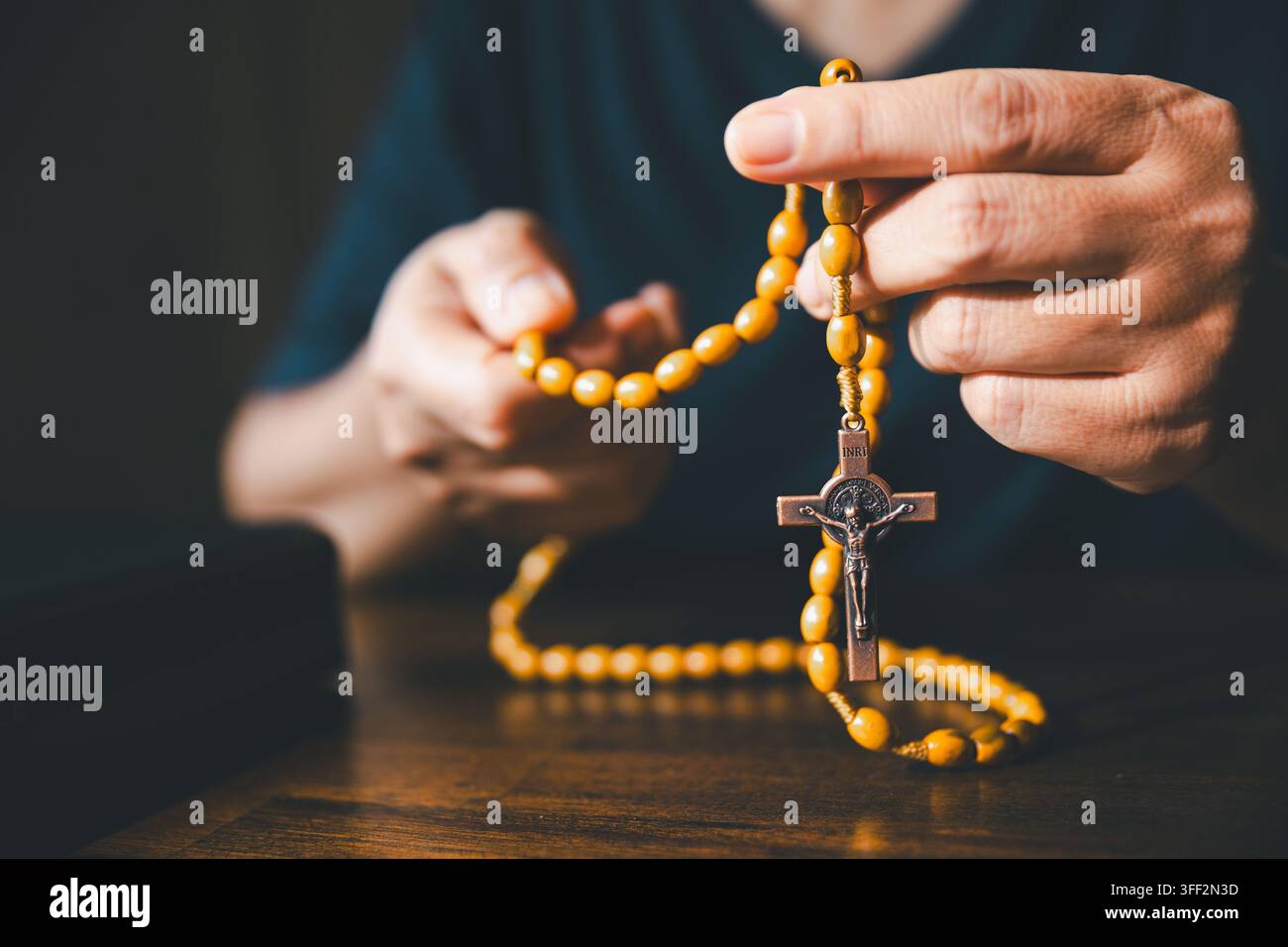 Close-up de mains tenant des chapelets et un crucifix dans une lumière dramatique, représentant la prière chrétienne et catholique, la foi, la dévotion, l'adoration, l'esprit Banque D'Images