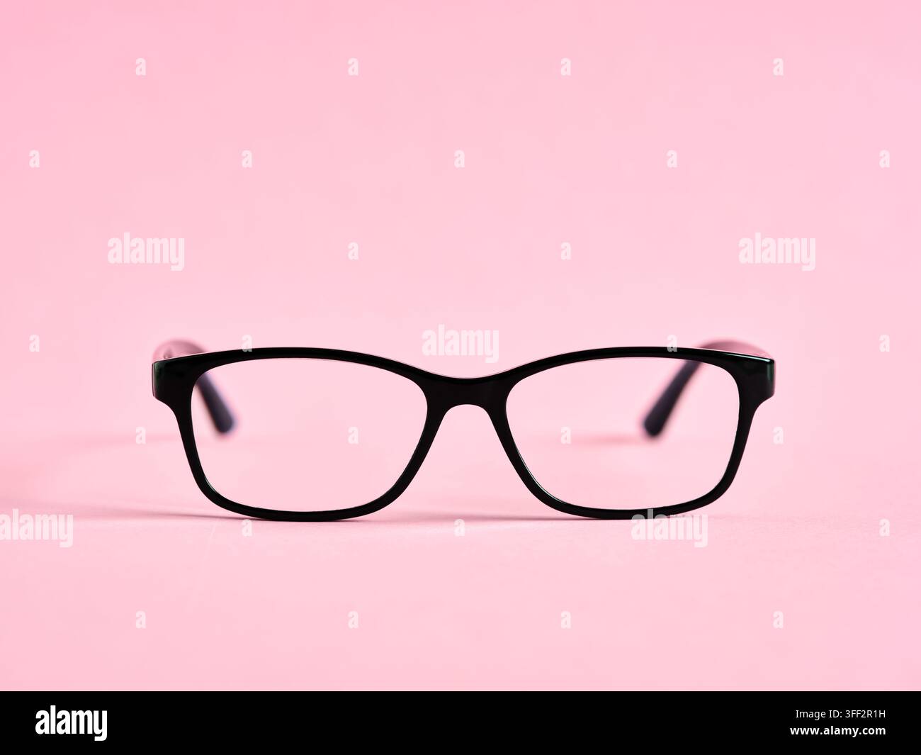 Lunettes à monture noire posées sur un fond rose, représentant la vision et le style Banque D'Images