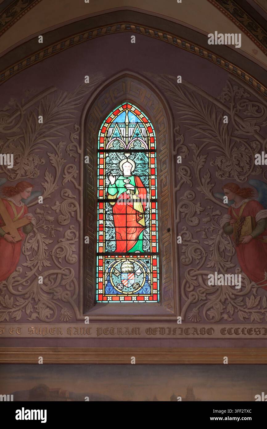 Une fenêtre en vitrail cintrée représentant une figure religieuse est encastrée dans une alcôve en plâtre finement sculptée à l'intérieur d'une église. Banque D'Images