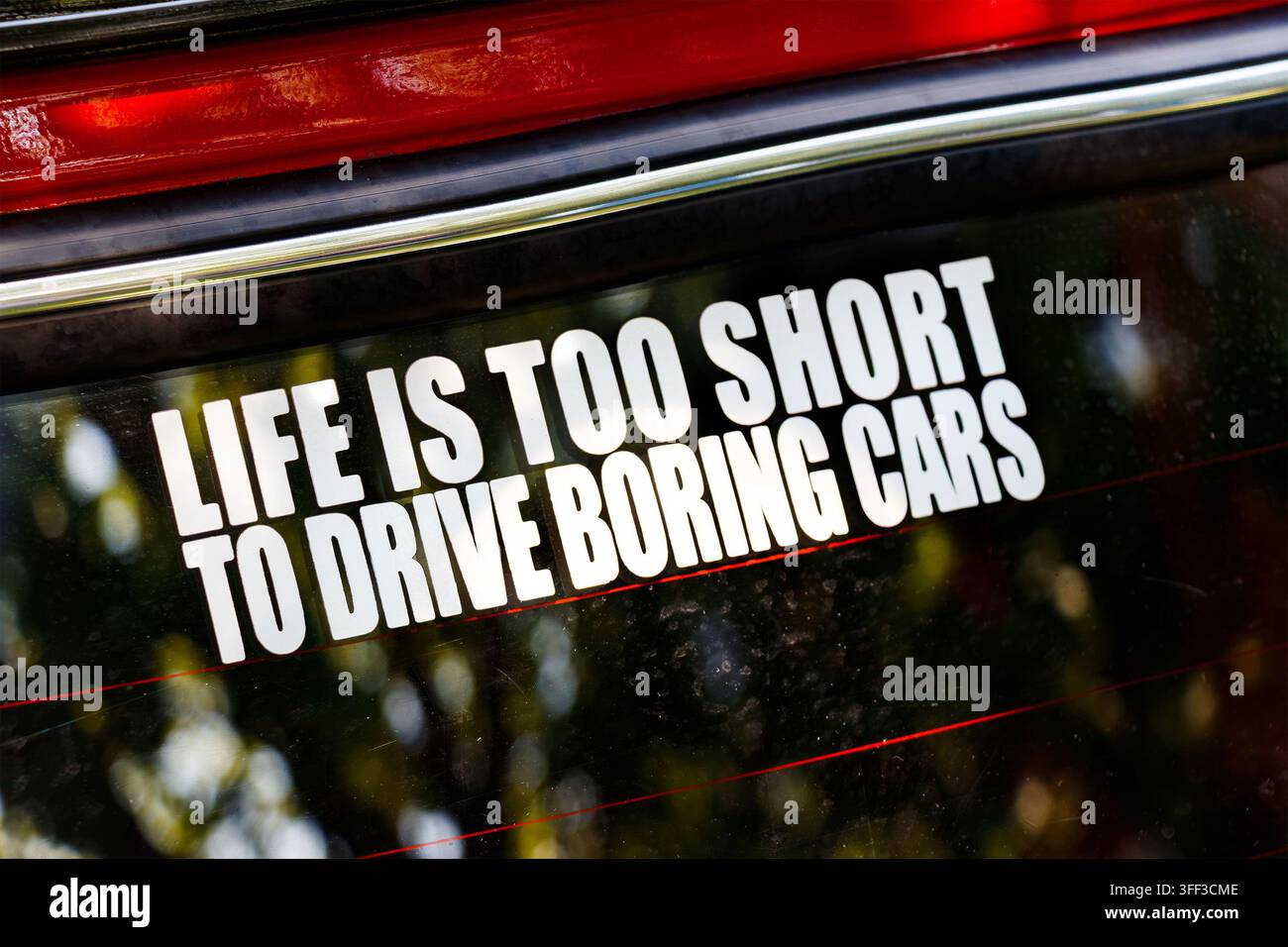 Autocollant portant l'inscription « LIFE IS TOO SHORT TO DRIVE BORING CARS » sur la vitre arrière d'un véhicule garé en ville Banque D'Images