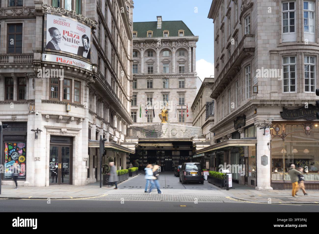 Les piétons marchent le long de Savoy Court pour visiter le luxueux Savoy Hotel de Londres, arrivant à son entrée emblématique et à sa statue. Banque D'Images