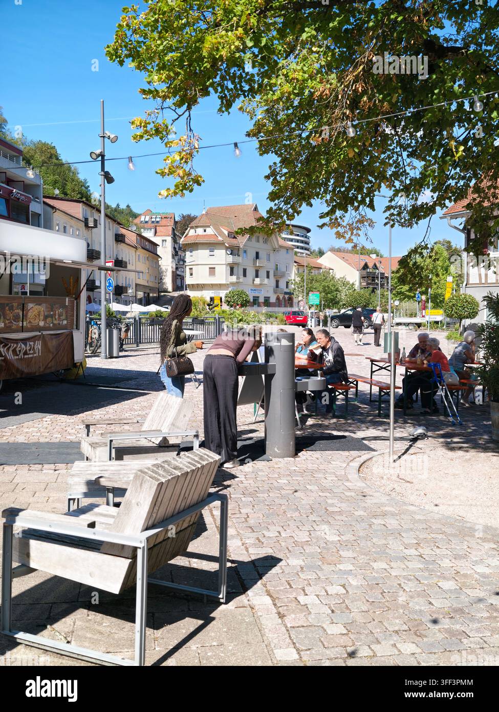 Bad Herrenalb, Allemagne, 5 septembre 2026 : place de restauration extérieure où des gens savourent des snacks de rue et des boissons sur des bancs et des tables à l’ombre des arbres Banque D'Images