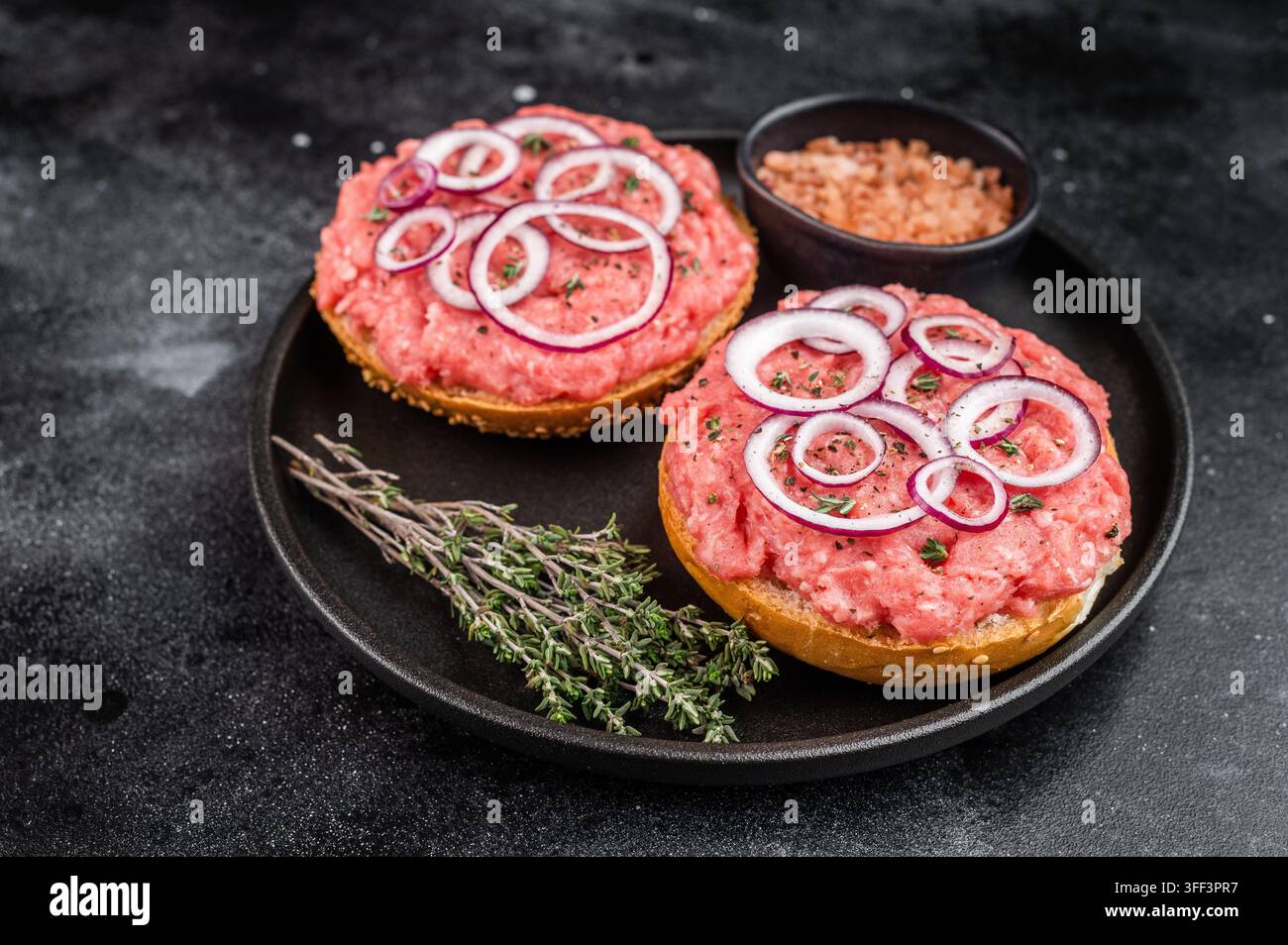 Mettbroetchen sandwichs de porc allemand avec porc haché cru étaler les rondelles d'oignon et les herbes sur une plaque noire. Banque D'Images