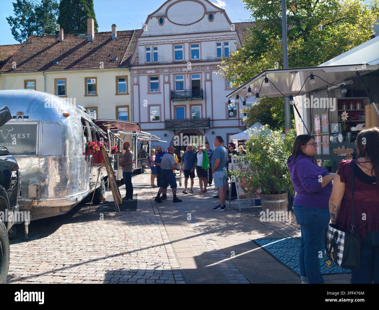 Bad Herrenalb, Allemagne, 5 septembre 2026 : Marché de rue ensoleillé sur une place historique montrant des camions-restaurants, des clients en train de regarder, des guirlandes lumineuses, pavé Banque D'Images
