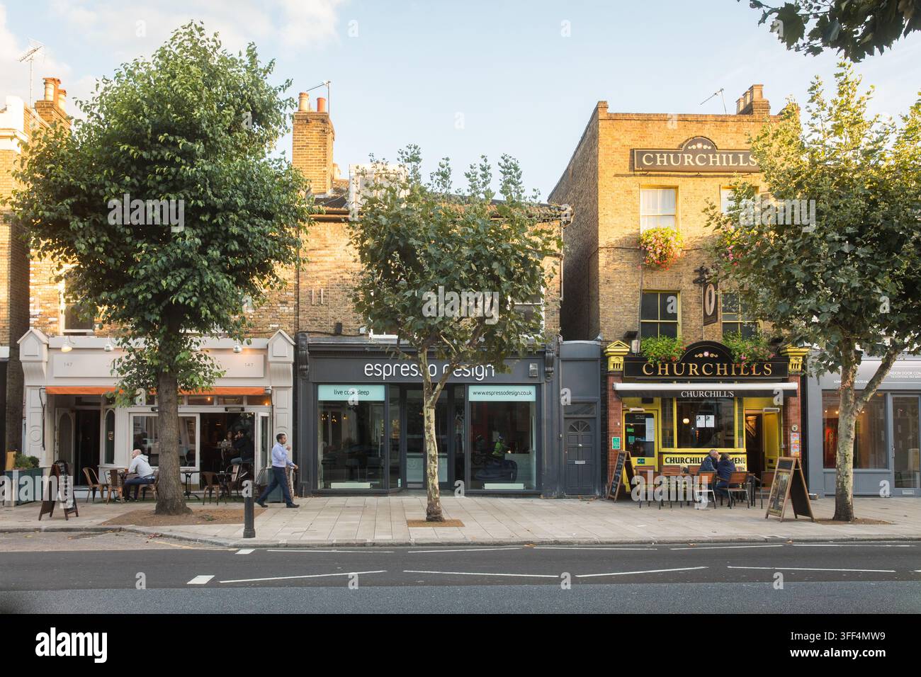 Les piétons passent devant Espresso Design et les clients sont assis à l'extérieur du pub Churchills sur St John's Hill, à Londres, profitant d'une journée ensoleillée. Banque D'Images