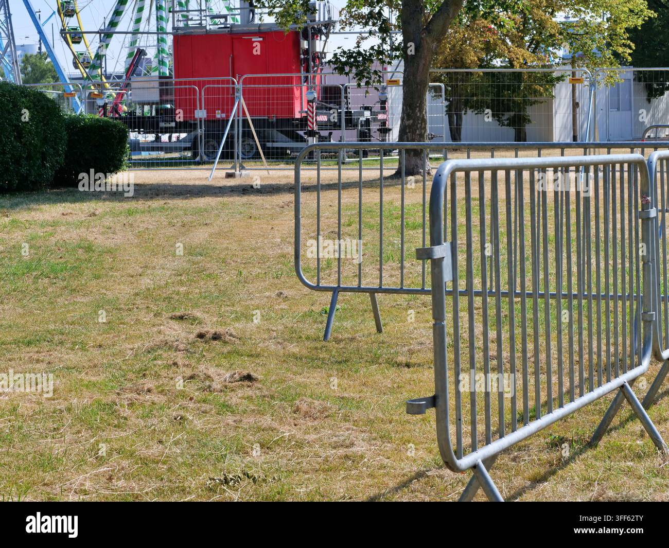 Perspective en gros plan de barricades métalliques de contrôle de foule installées sur de l'herbe sèche dans un terrain de carnaval ou de parc d'attractions. À l'arrière-plan, des remorques rouges et Banque D'Images