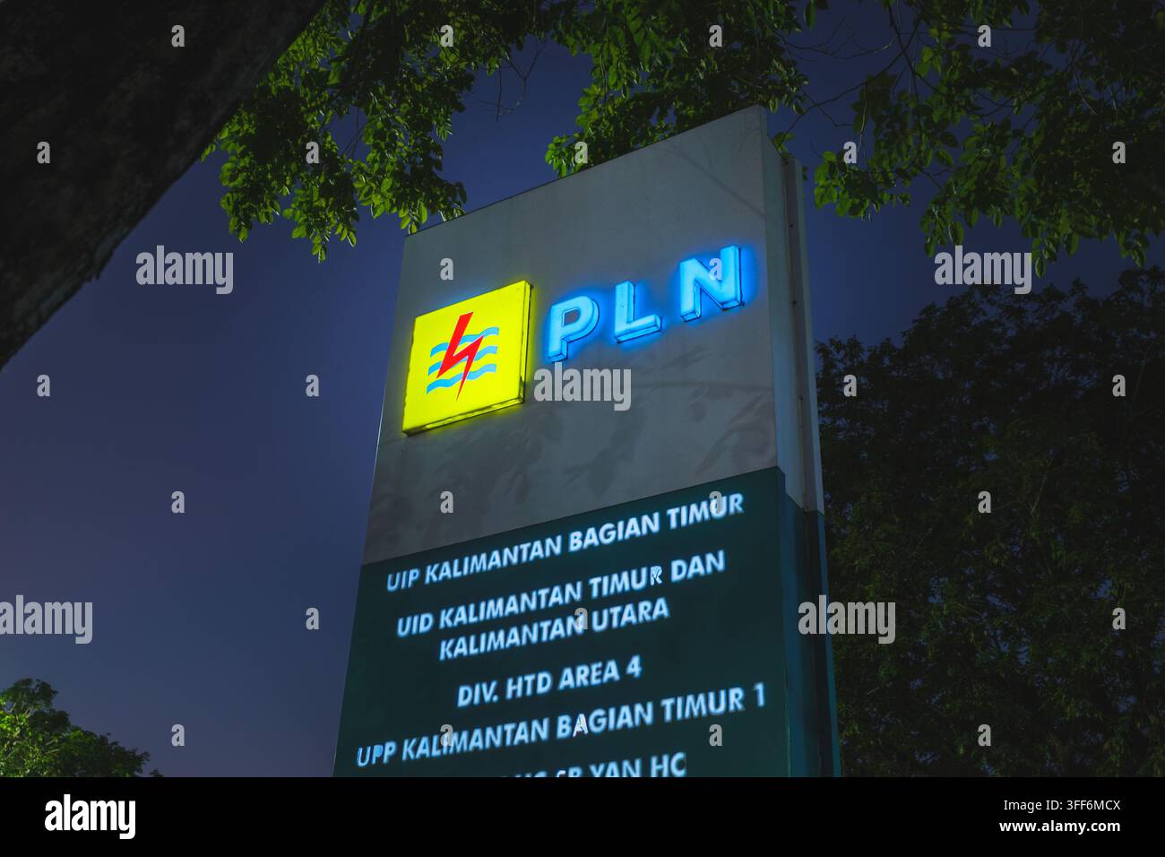 Balikpapan, Indonésie - 7 août 2026. Gros plan vertical d'un panneau d'entreprise illuminé pour PLN contre un ciel nocturne sombre. Banque D'Images
