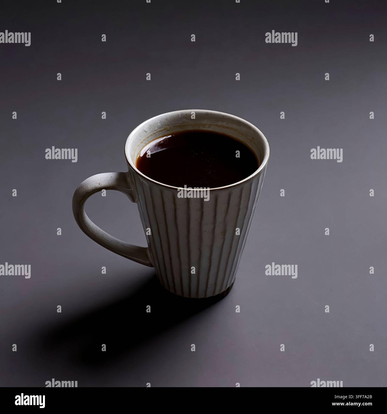 Café noir chaud dans une grande tasse en céramique cannelée sur un fond minimaliste sombre avec un éclairage dramatique Banque D'Images
